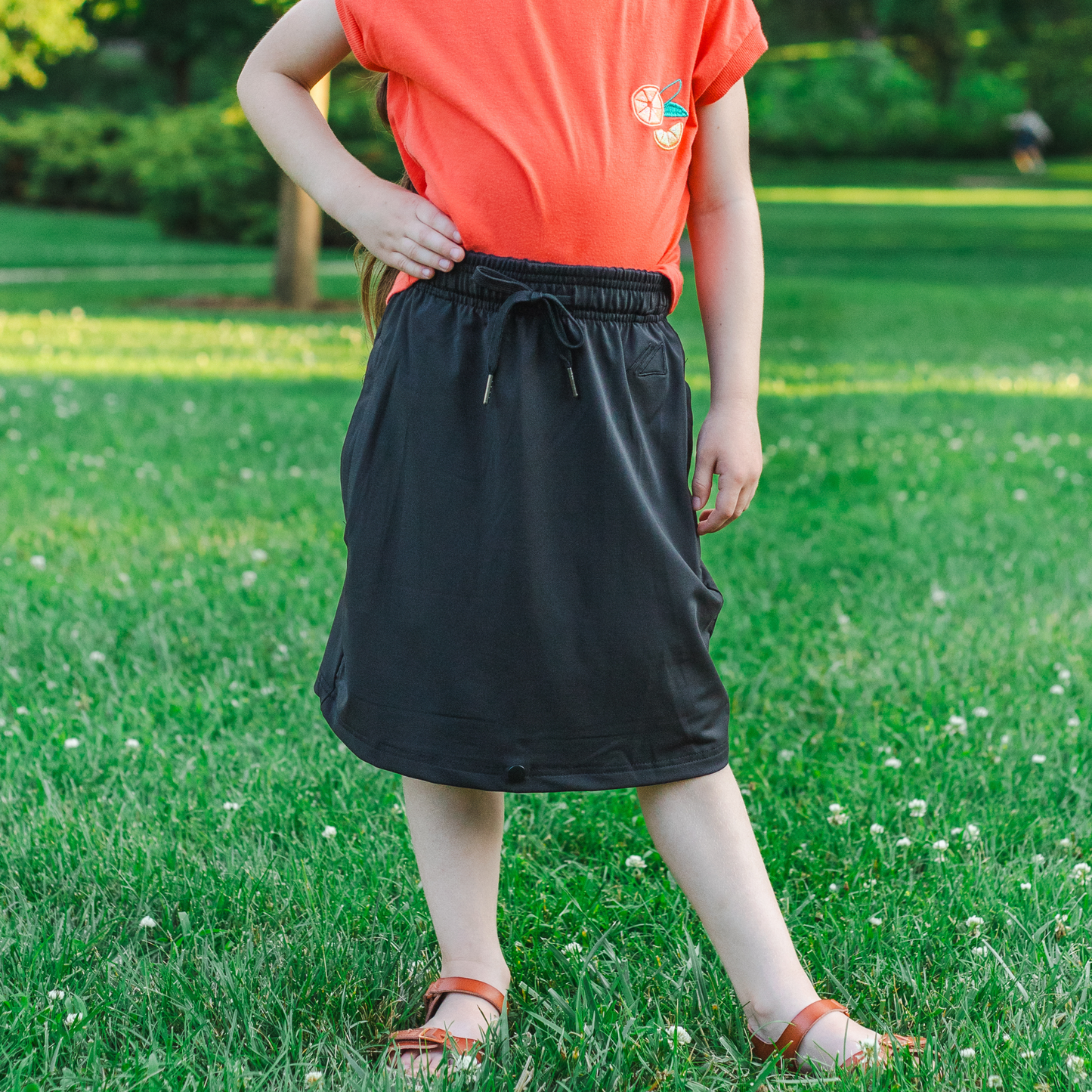 Kid wearing a black skirt and orange shirt standing on grass