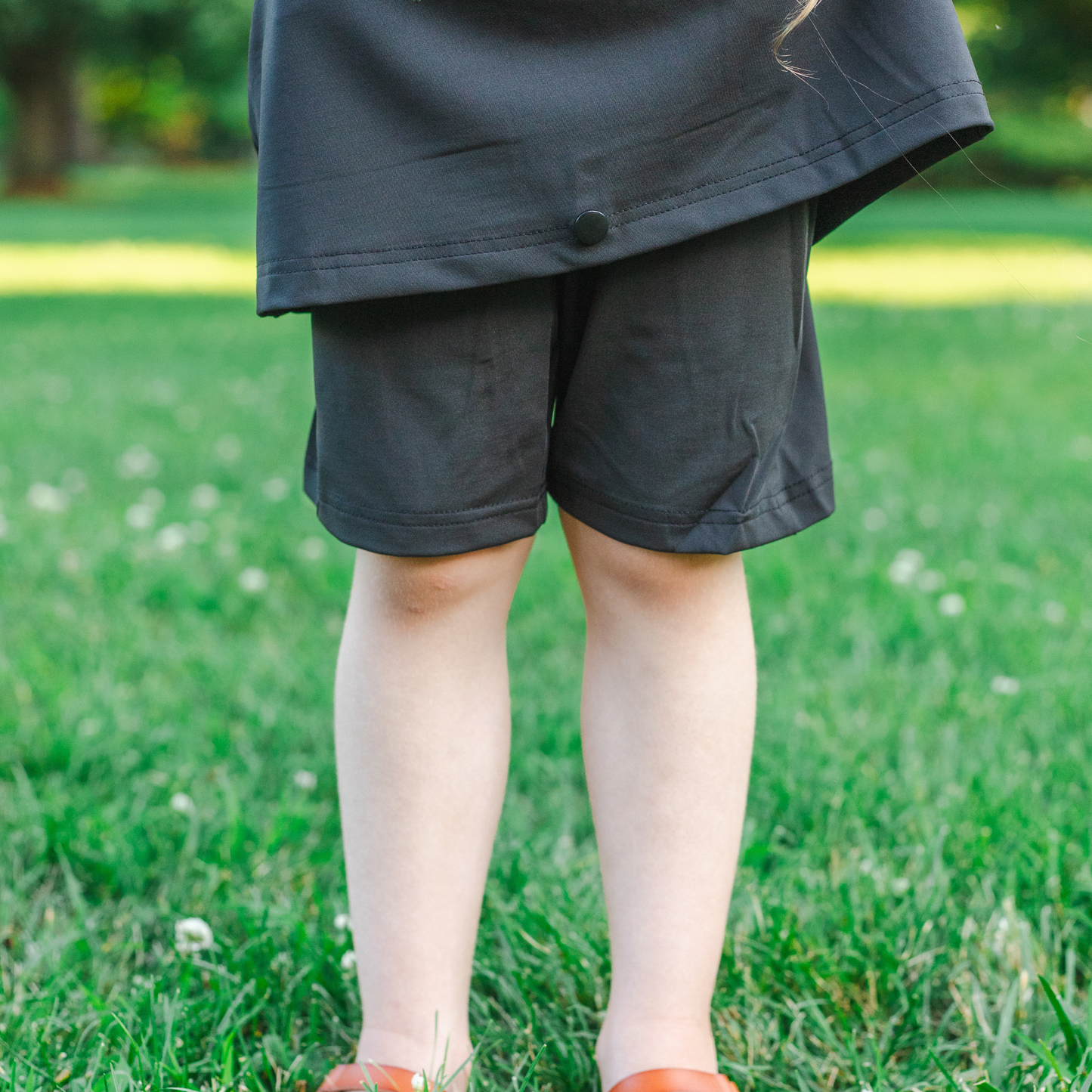 
                  
                    Kid wearing black skirt with shorts standing on grass
                  
                