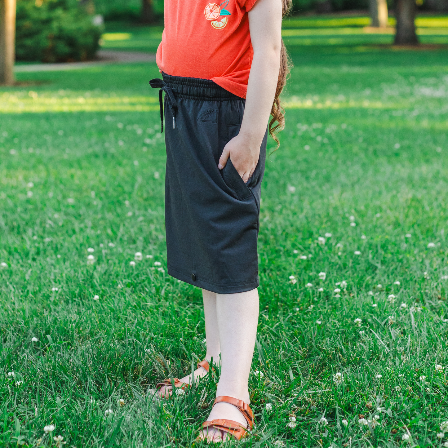 Kid wearing a red shirt and black skirt standing on grass