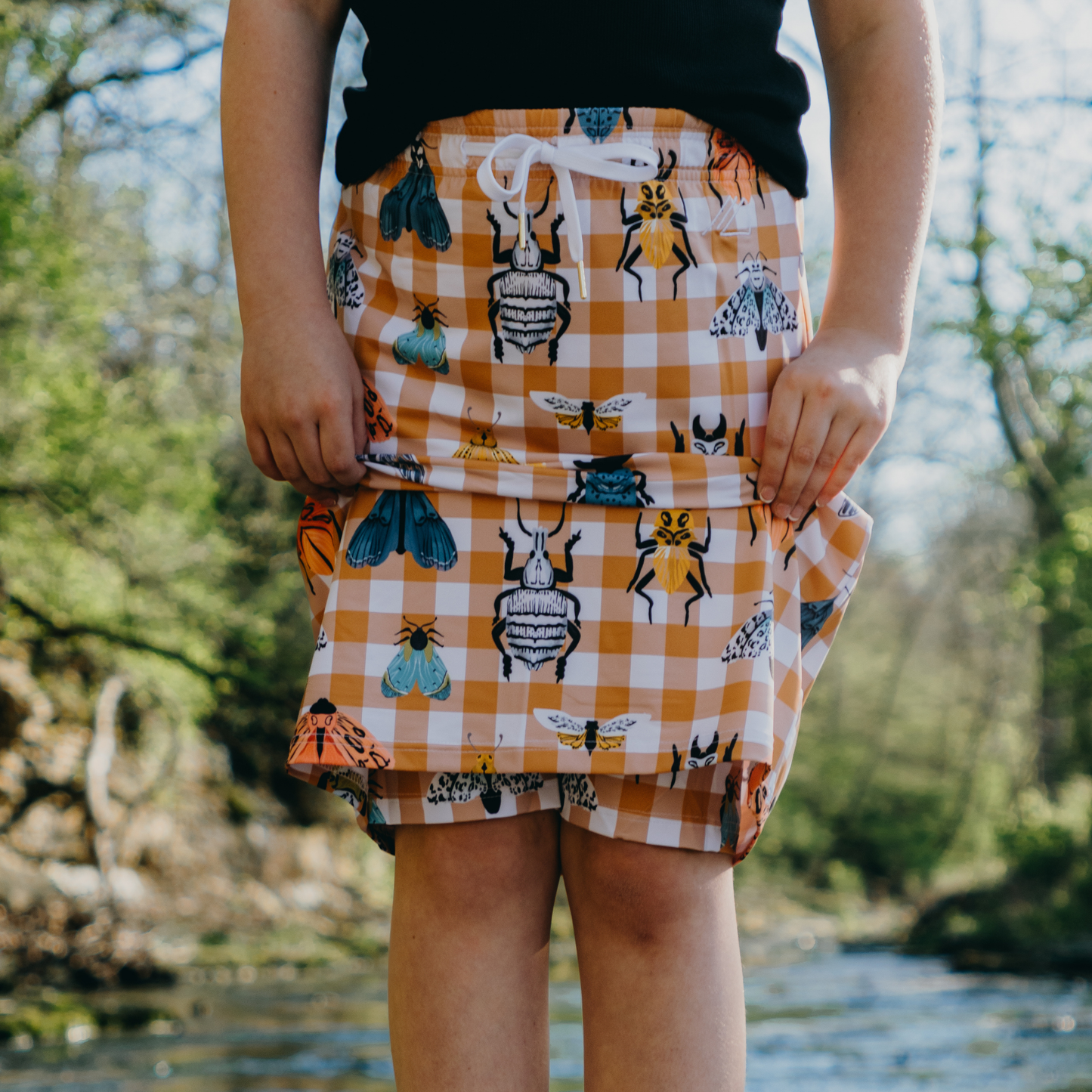 
                  
                    Kid wearing a checkered skirt with insect patterns outdoors
                  
                