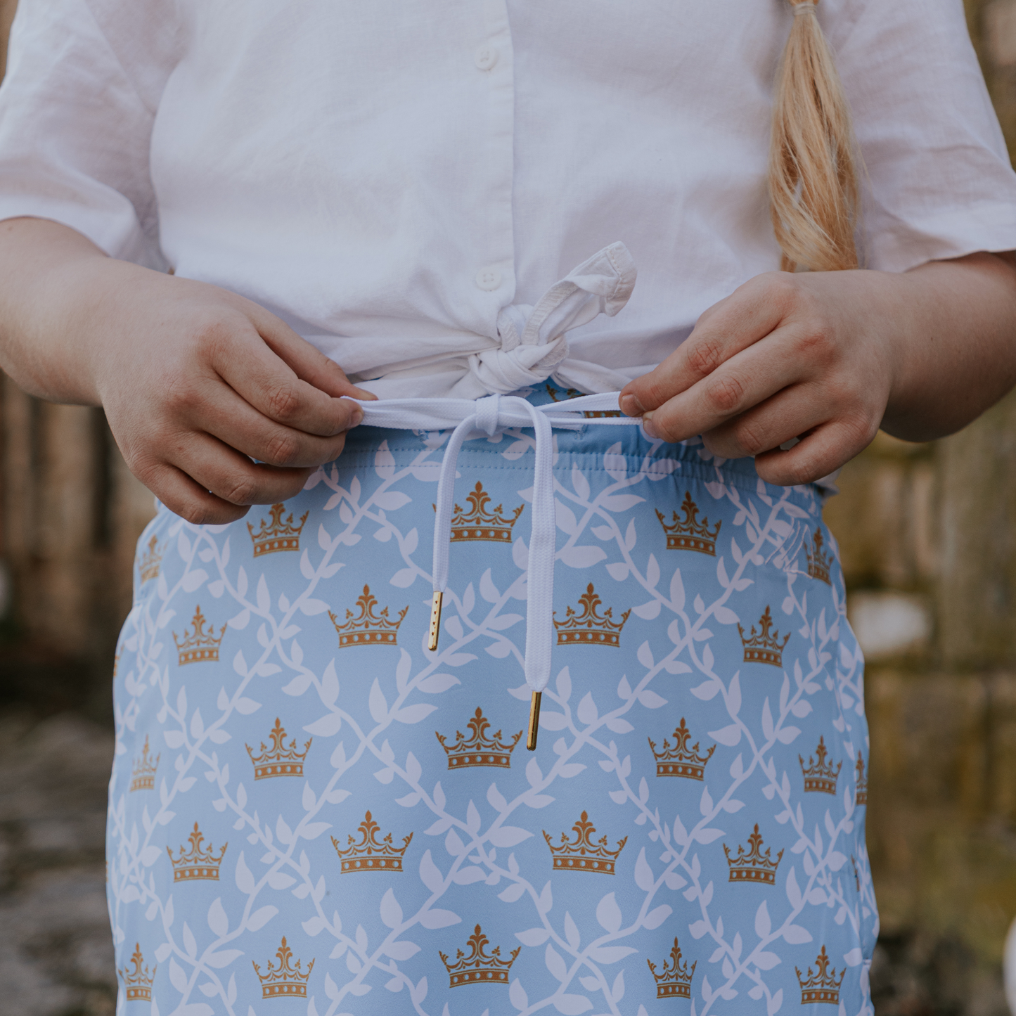 
                  
                    Person wearing a blue skirt with gold crown patterns, standing outdoors.
                  
                