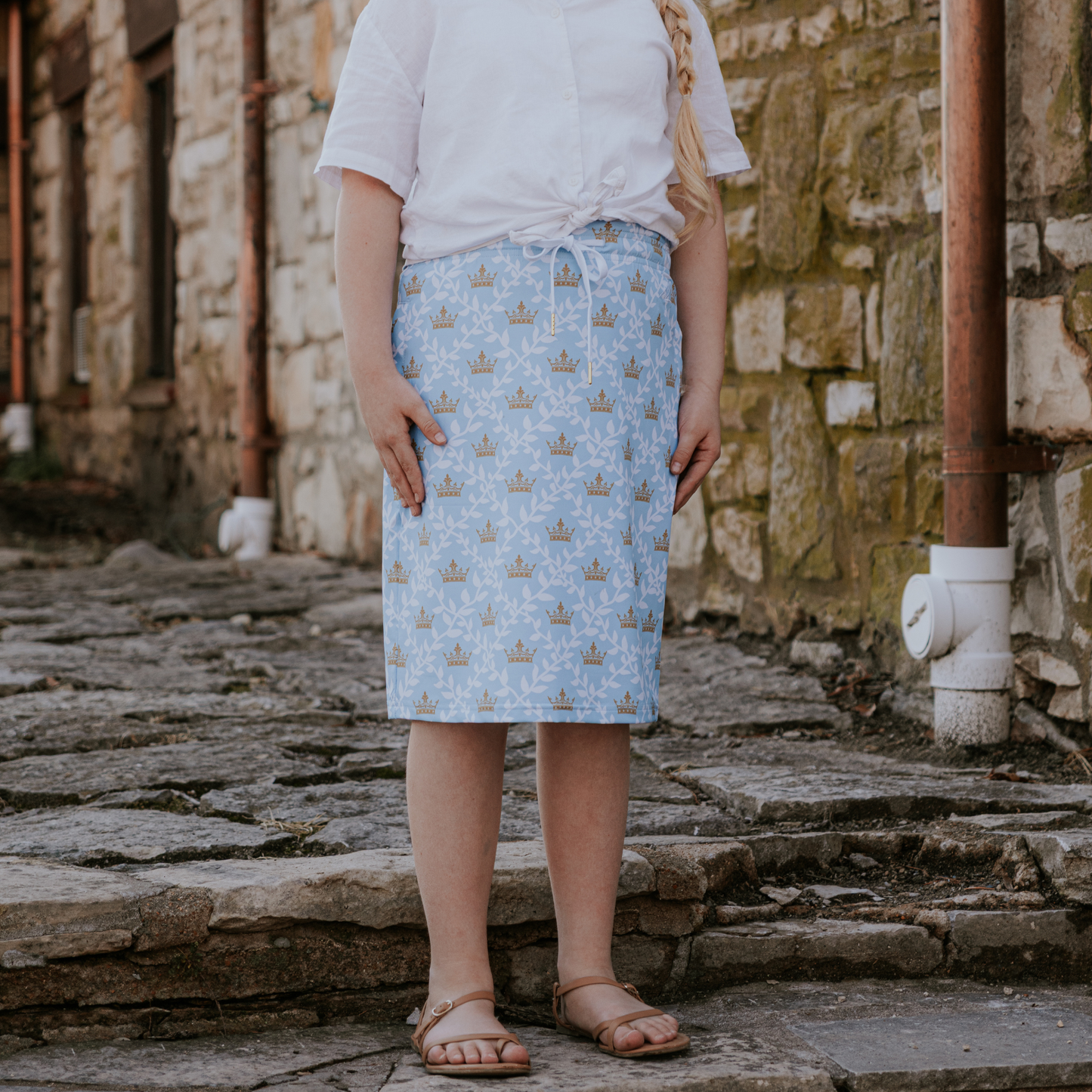 Person wearing a light blue skirt with a pattern, standing on stone steps against a stone wall.