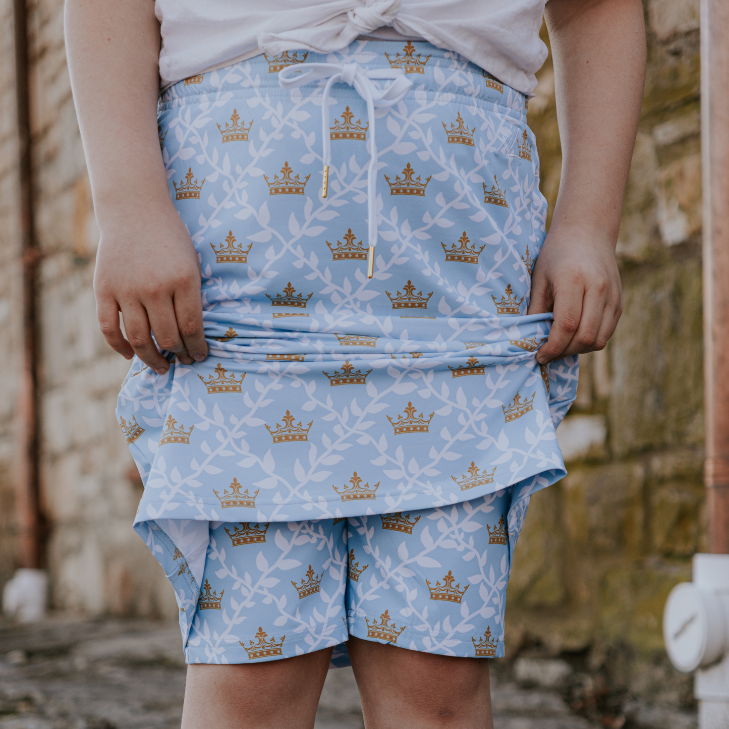 
                  
                    Person wearing a blue patterned skirt with crowns and leaves.
                  
                