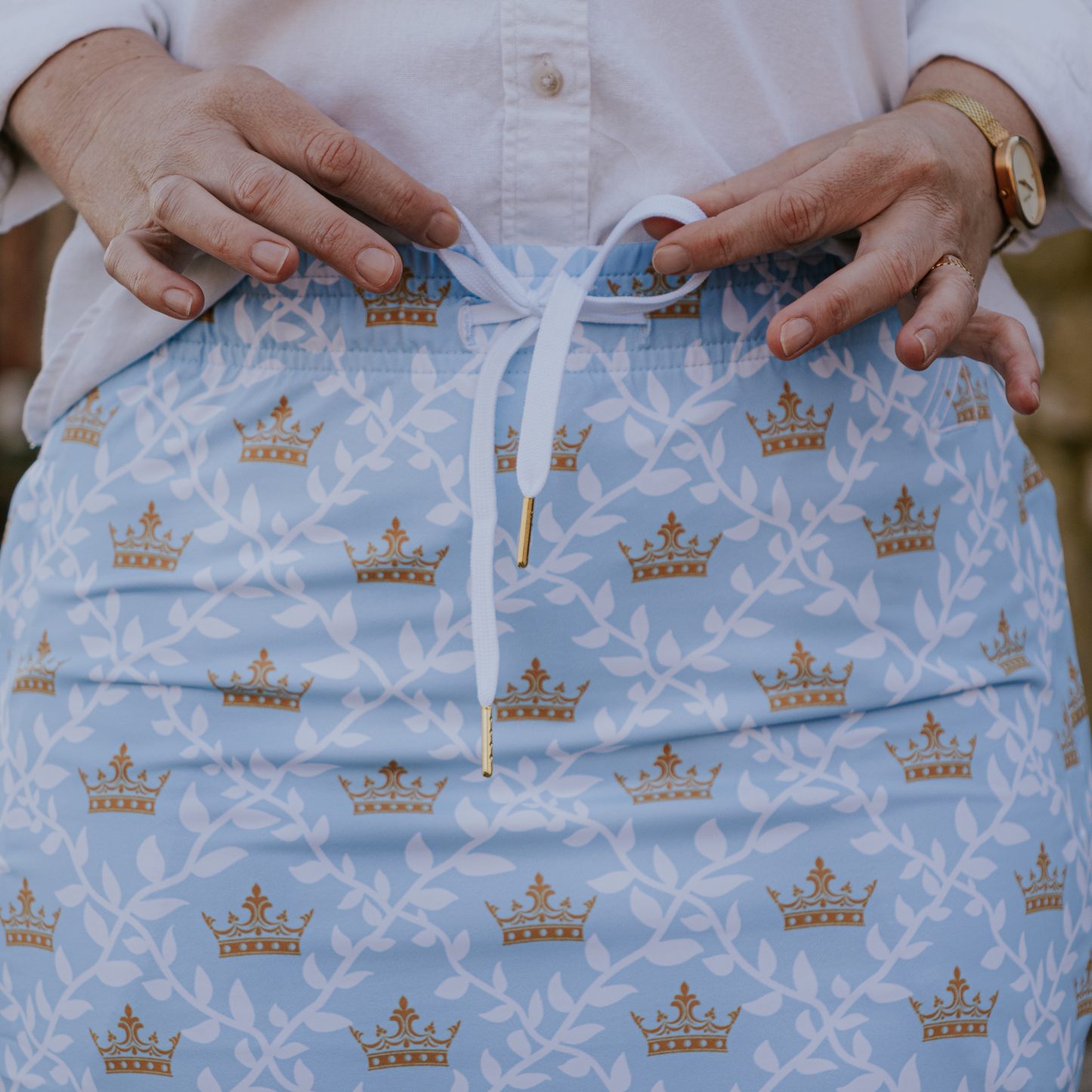 
                  
                    Light blue skirt with gold crown pattern held by a person.
                  
                