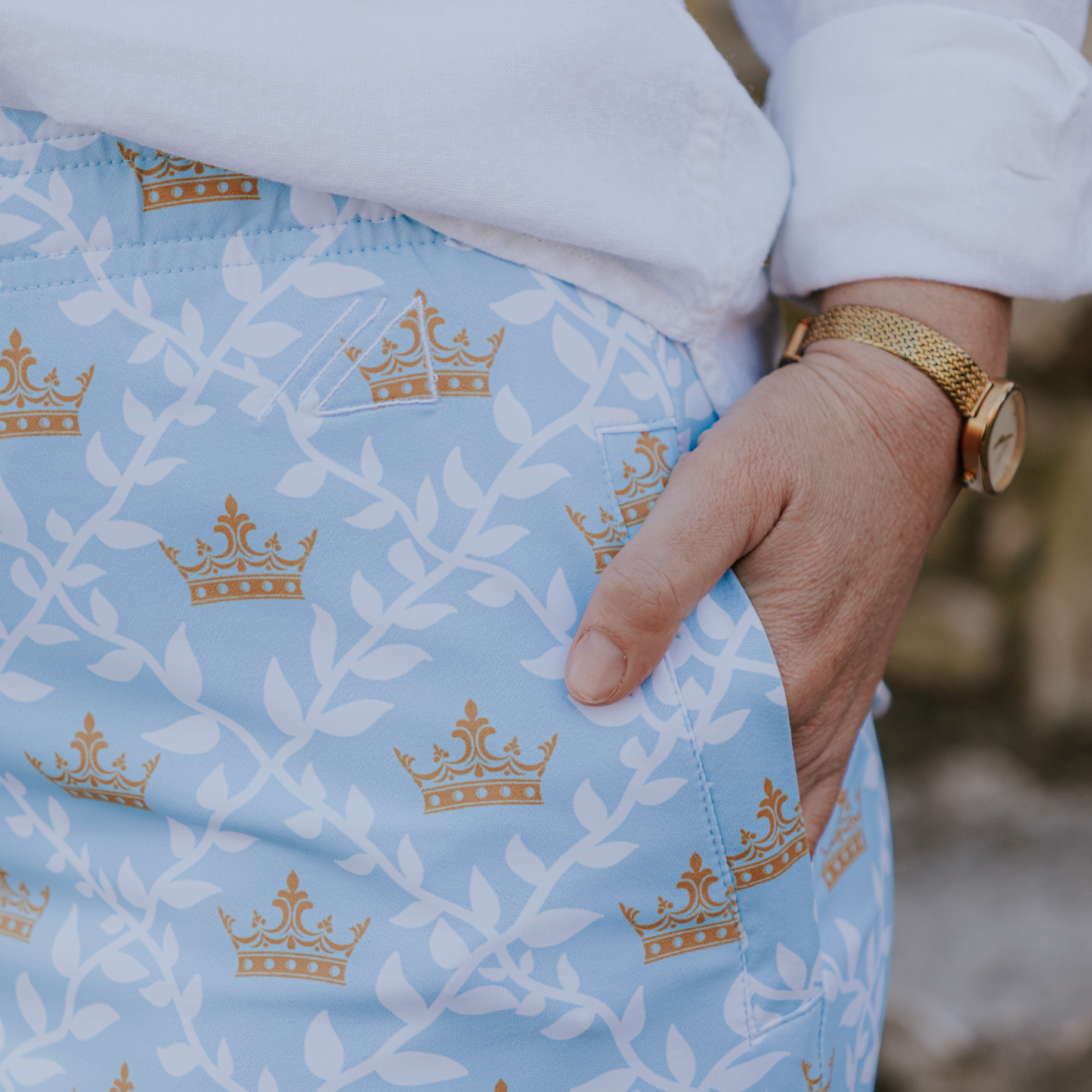 
                  
                    Light blue fabric with gold crown pattern with a pocket worn by a person wearing a white shirt and gold watch.
                  
                
