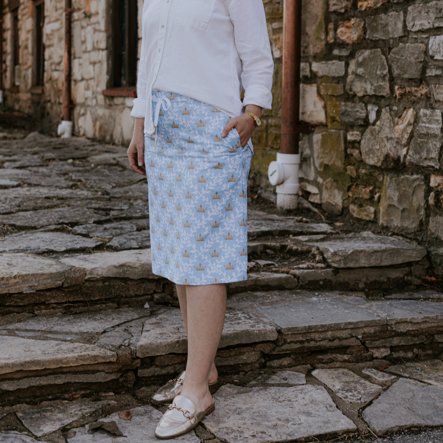 
                  
                    Person wearing a light blue skirt with a pattern standing on stone steps.
                  
                