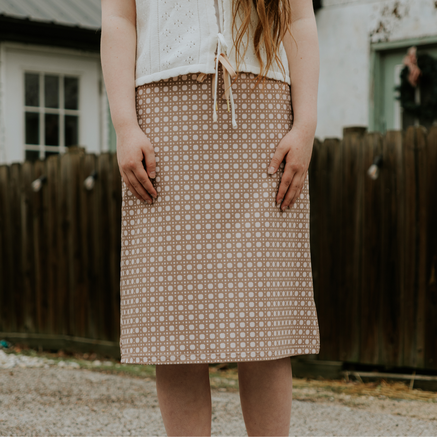 Person wearing a patterned skirt standing outdoors with a wooden fence in the background