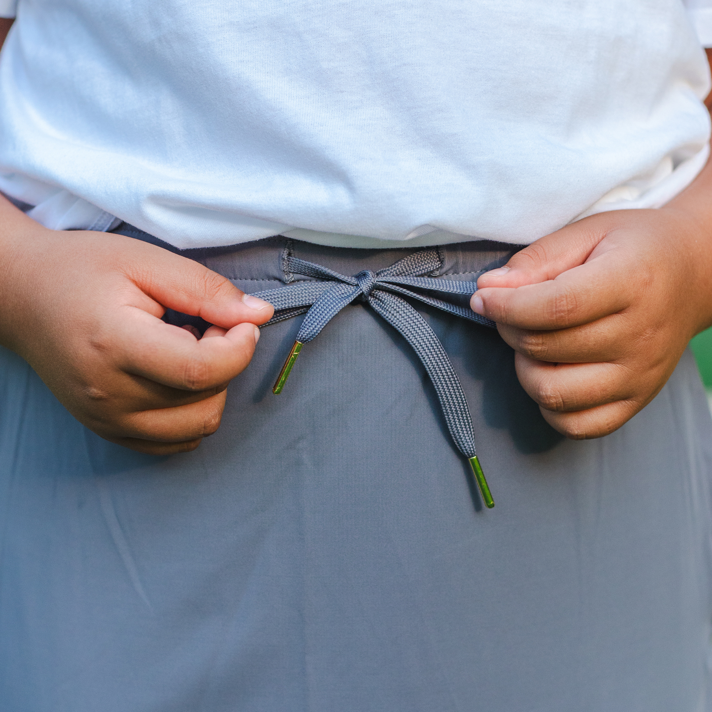 
                  
                    Kid tying a gray drawstring around their waist with a white shirt and light gray skirt.
                  
                
