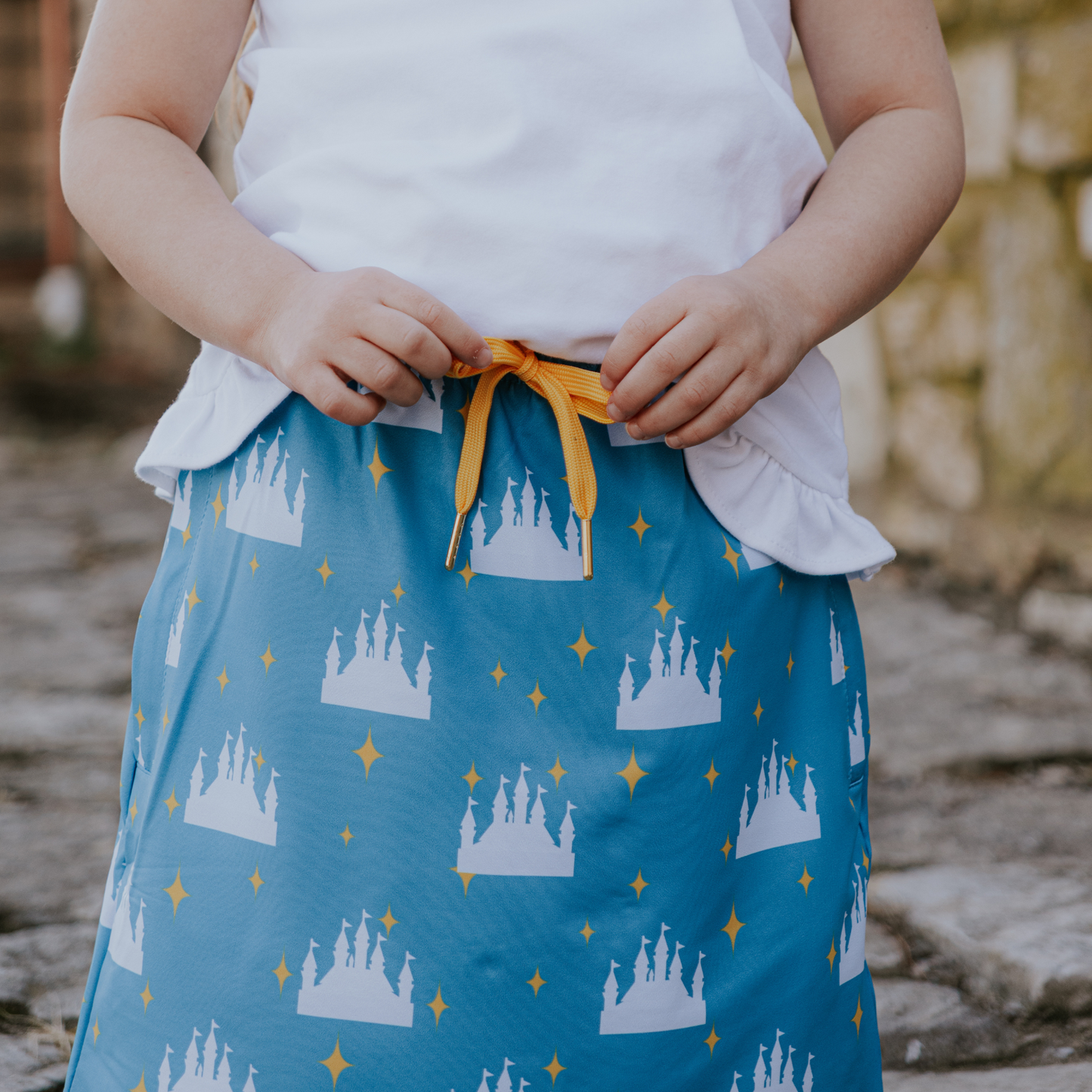 Child wearing a blue skirt with castle pattern and white top outdoors.