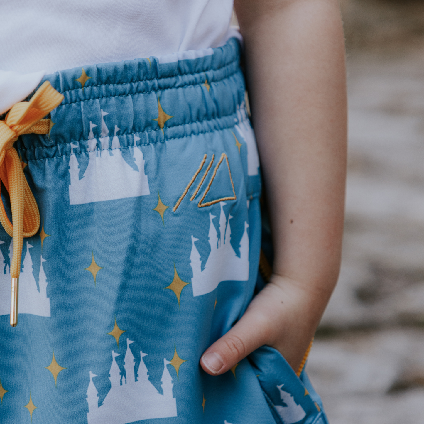 
                  
                    Blue shorts with castle pattern and yellow accents worn by a kid.
                  
                