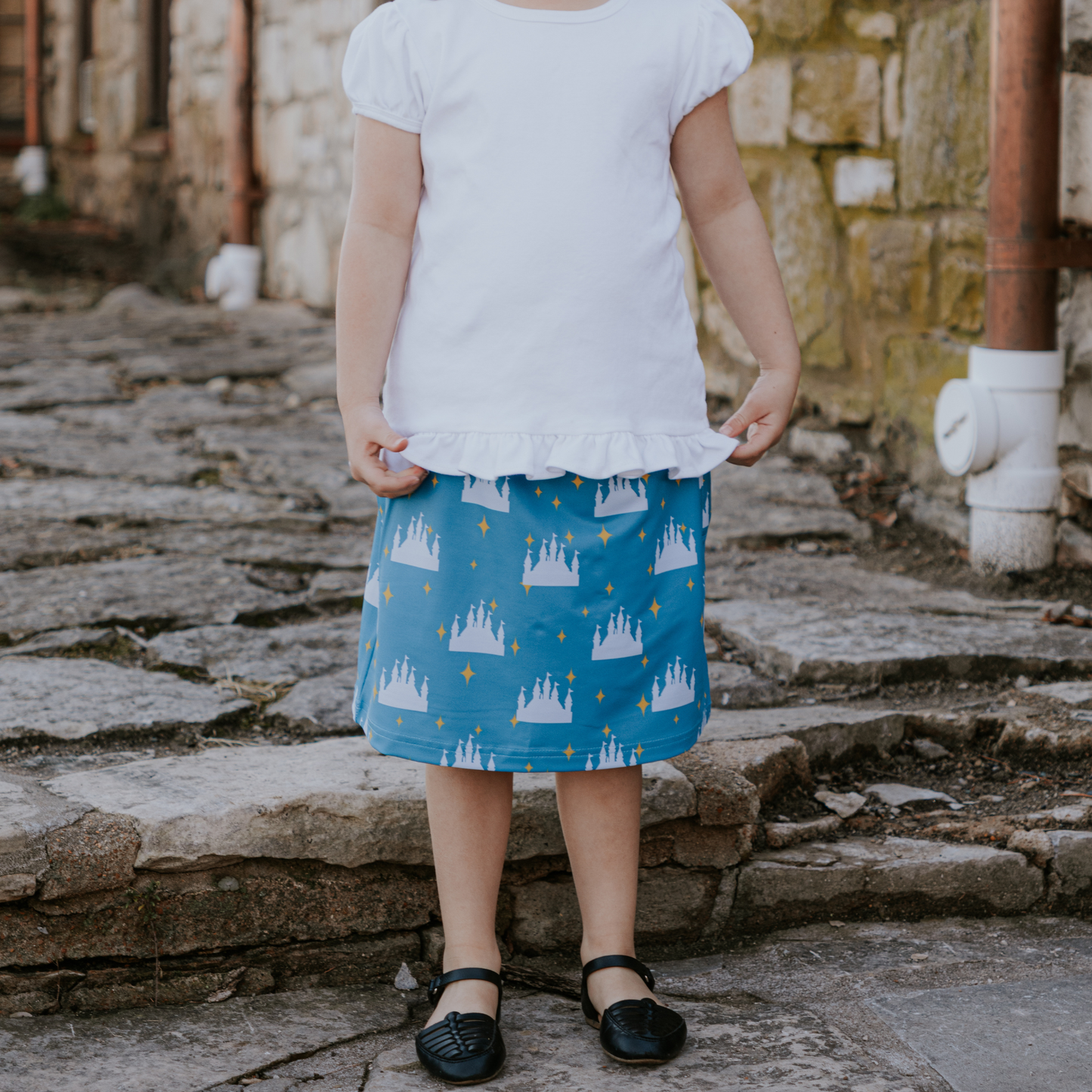 Child wearing a white top and blue skirt with castle pattern on stone steps.