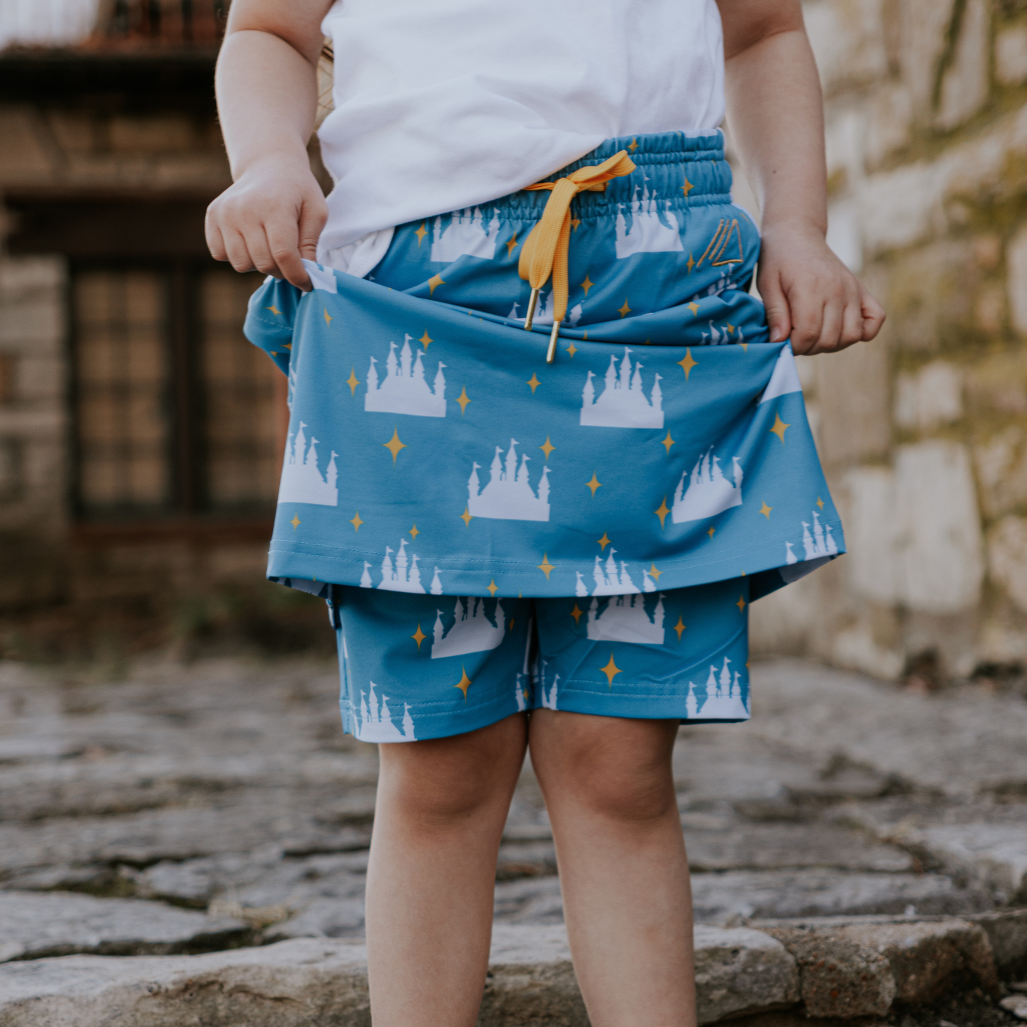 
                  
                    Child wearing blue skirt and shorts with castle pattern outdoors
                  
                