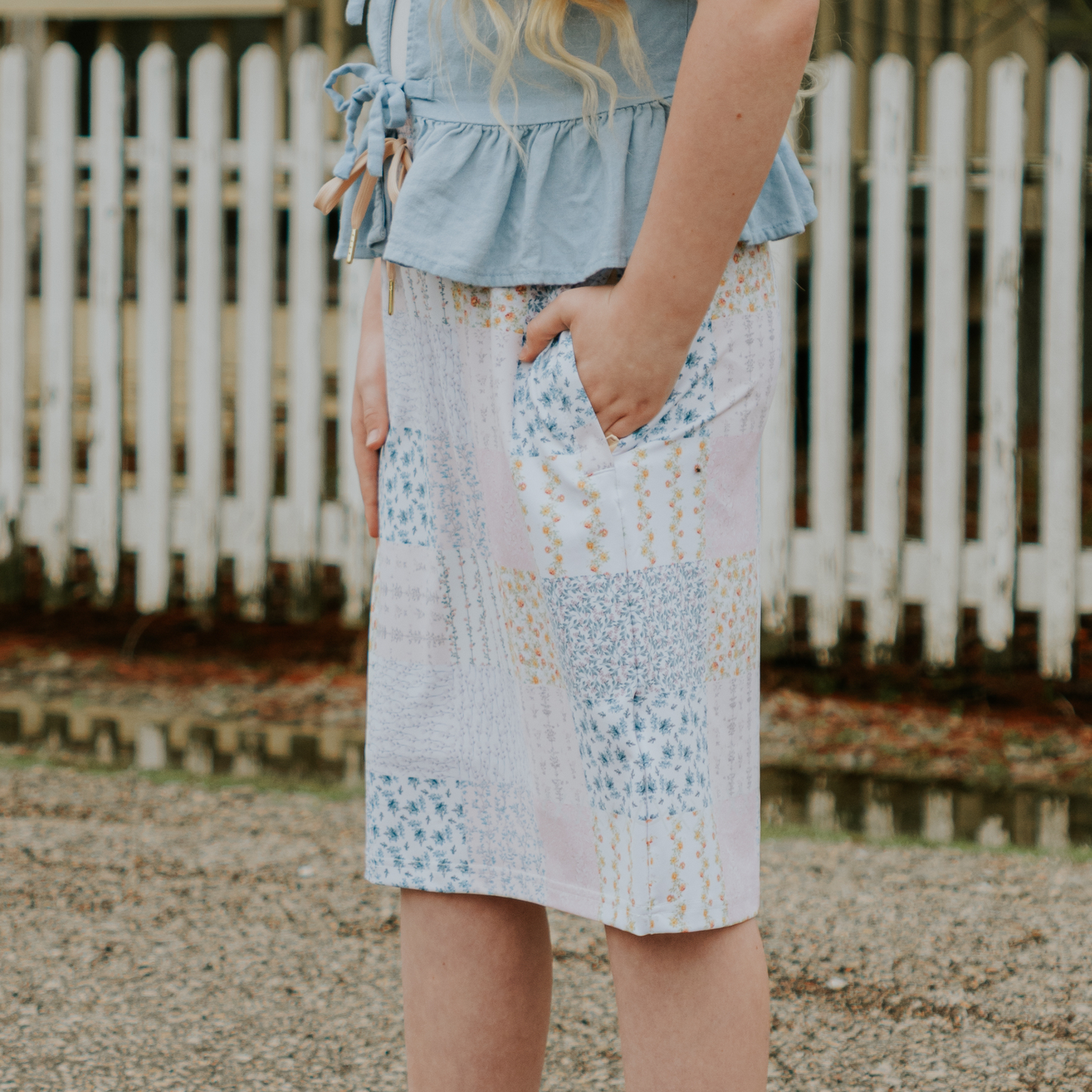
                  
                    Person wearing a denim jacket and patterned skirt standing in front of a white picket fence.
                  
                