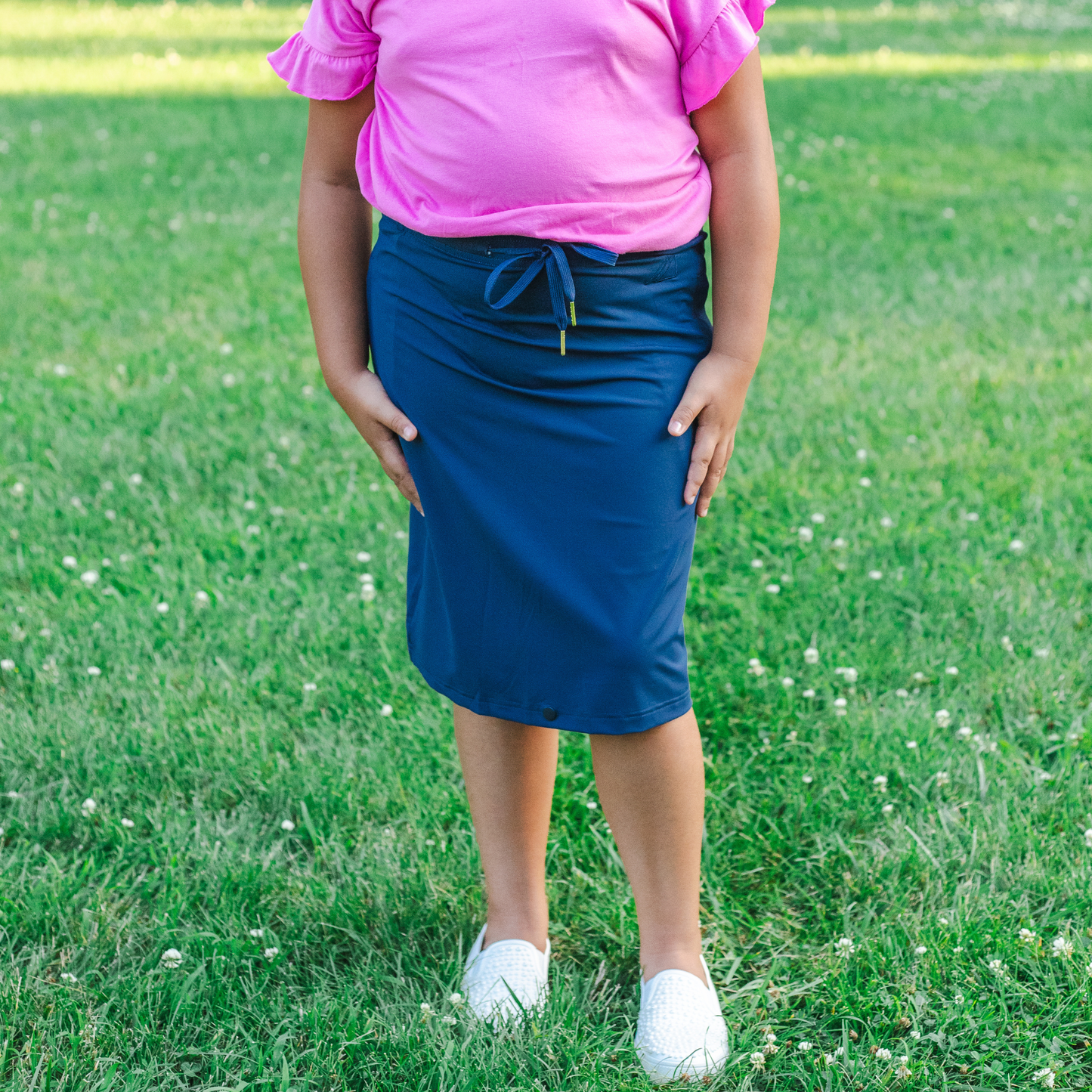 Kid wearing a pink shirt and blue skirt standing on grass