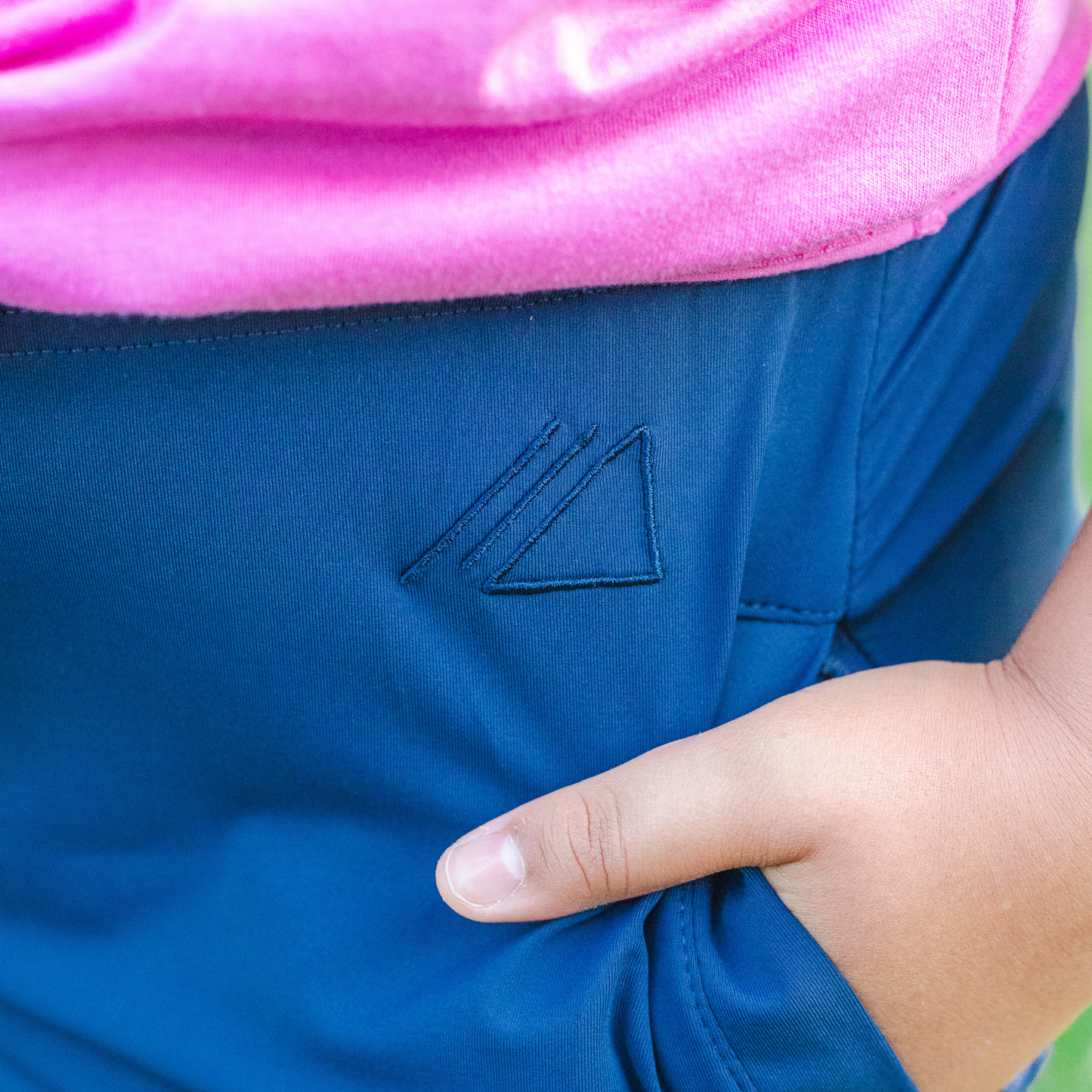 
                  
                    Blue skirt with a logo on the pocket, worn by a kid with a pink top.
                  
                