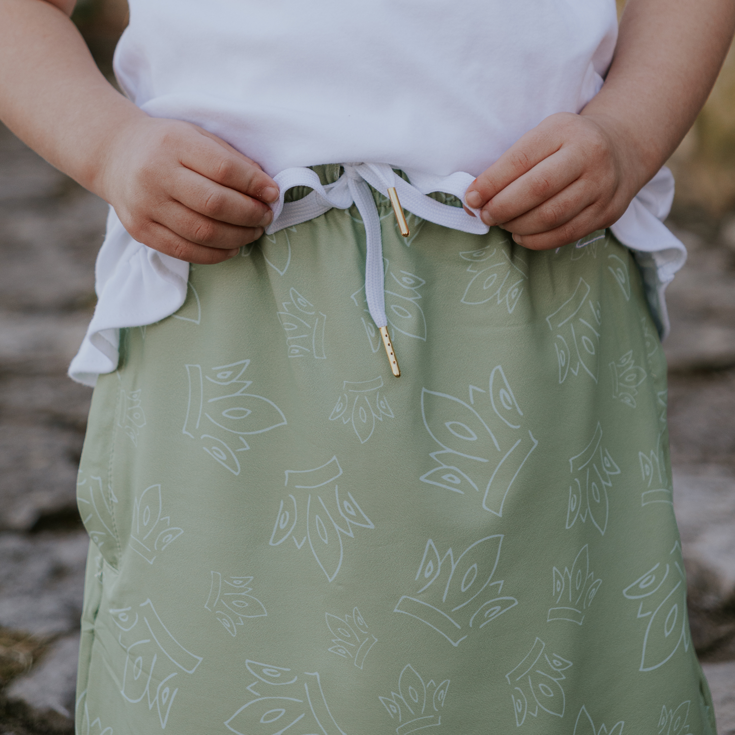 Person wearing a green skirt with white patterns and a white top, standing outdoors.