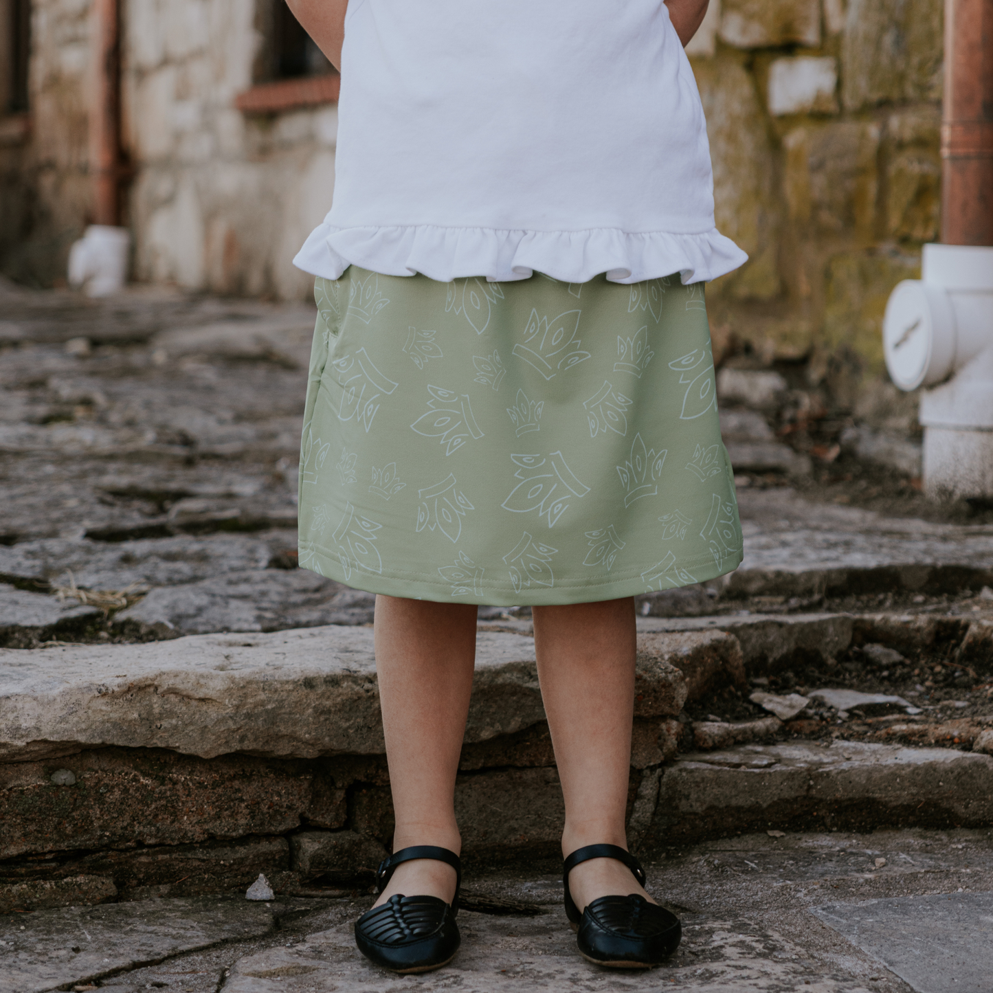 Person wearing a white top and green skirt with a pattern, standing on stone steps.