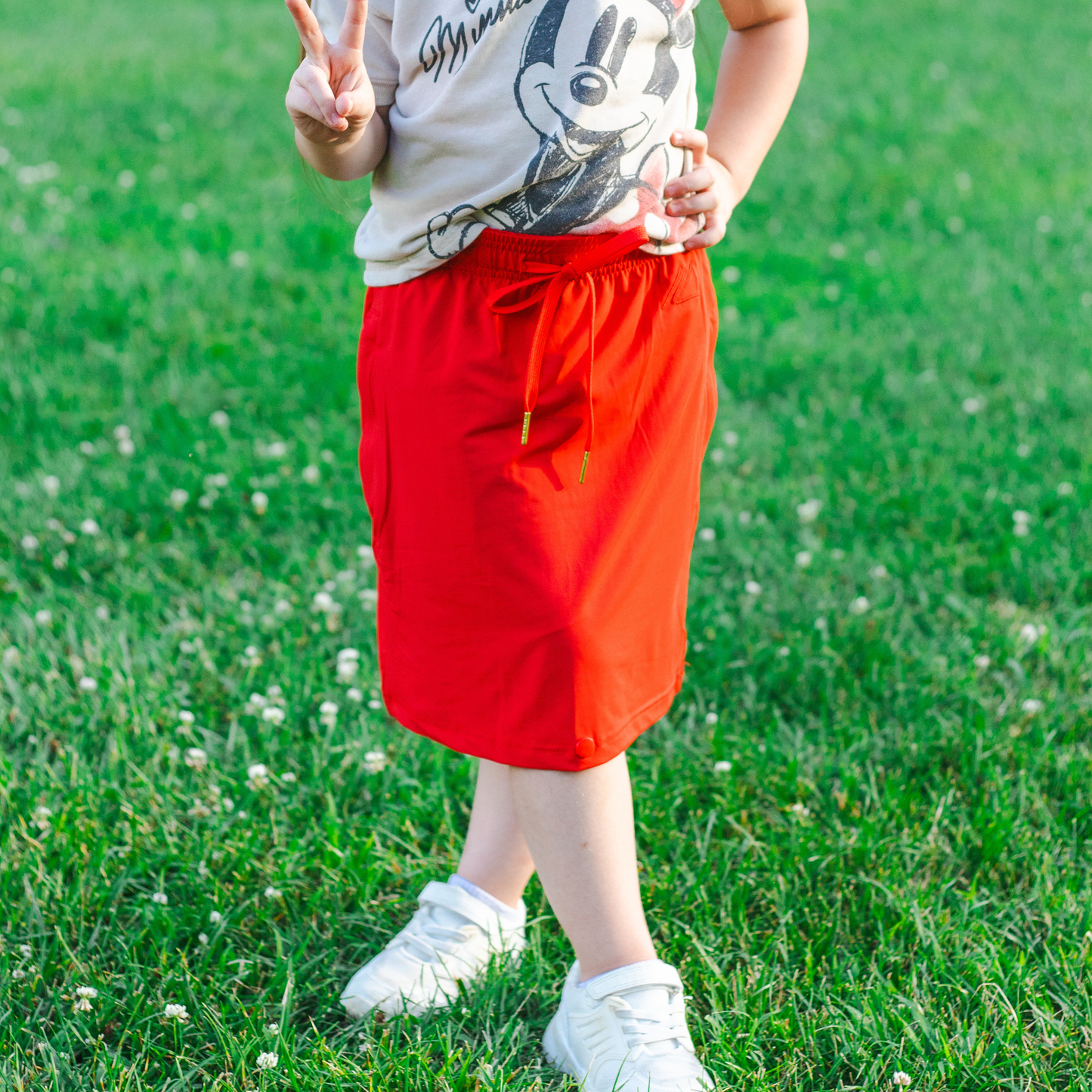 Kid wearing a red skirt and white shoes standing on grass