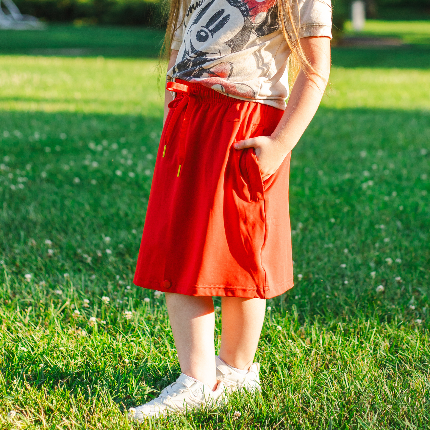Child wearing a red skirt and white shoes standing on grass