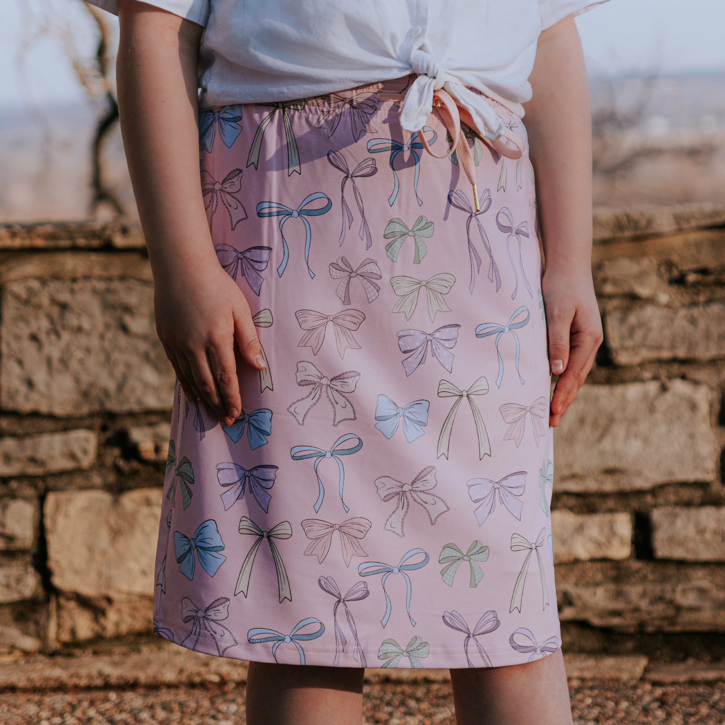 Person wearing a skirt with bow pattern against a stone wall.