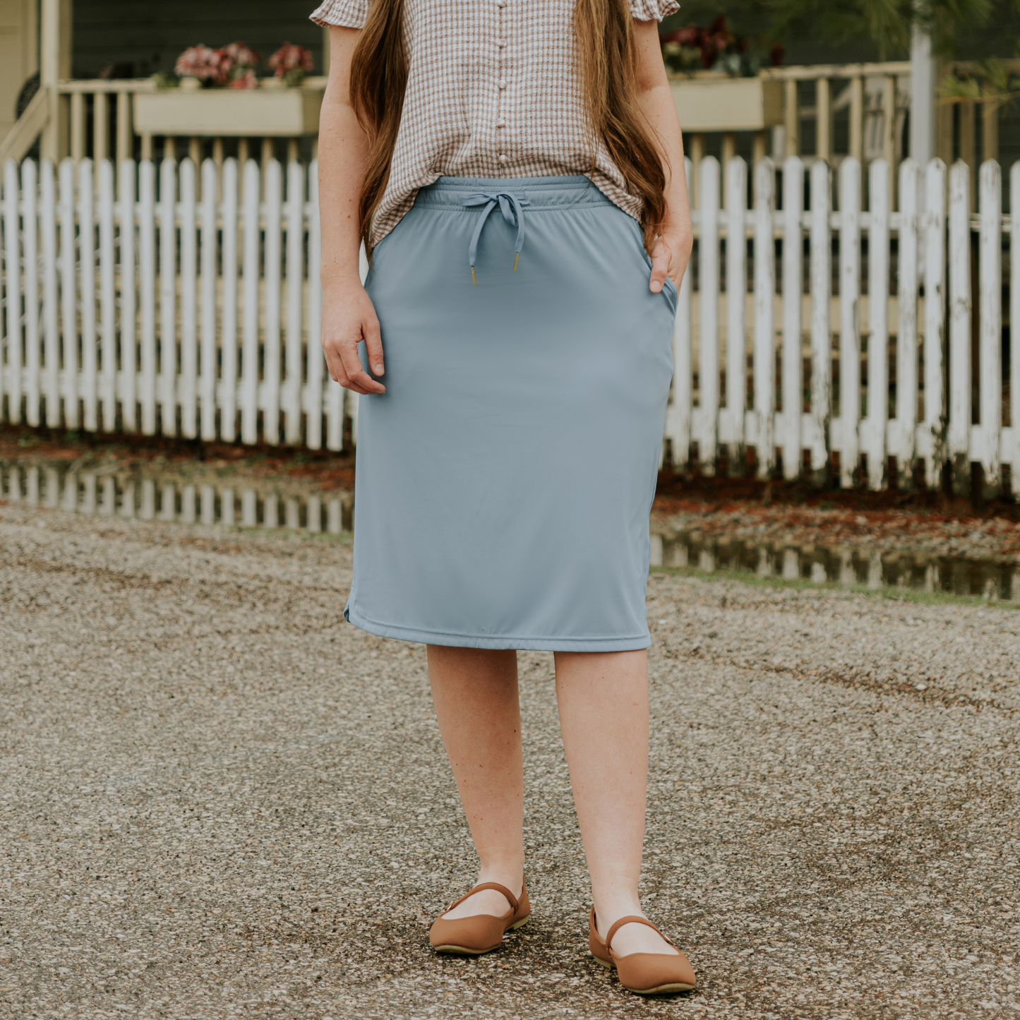 Person wearing a light blue skirt standing in front of a white picket fence.