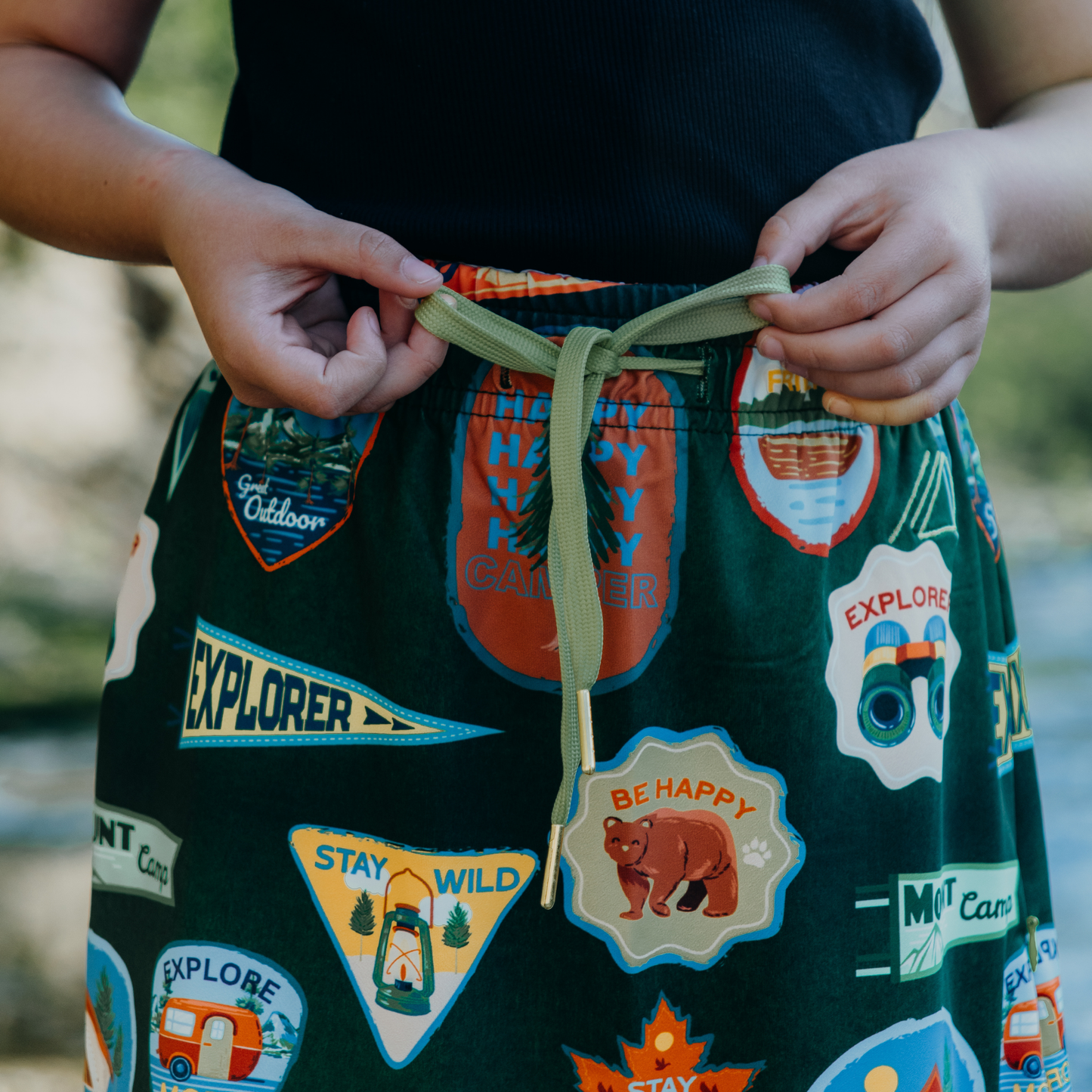 
                  
                    Kid wearing a green skirt with outdoor-themed patches and text.
                  
                