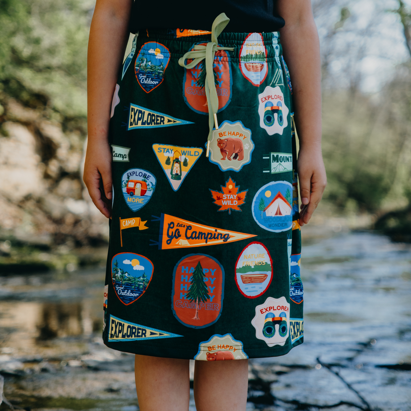 Kid wearing a skirt with camping-themed patches in a natural setting