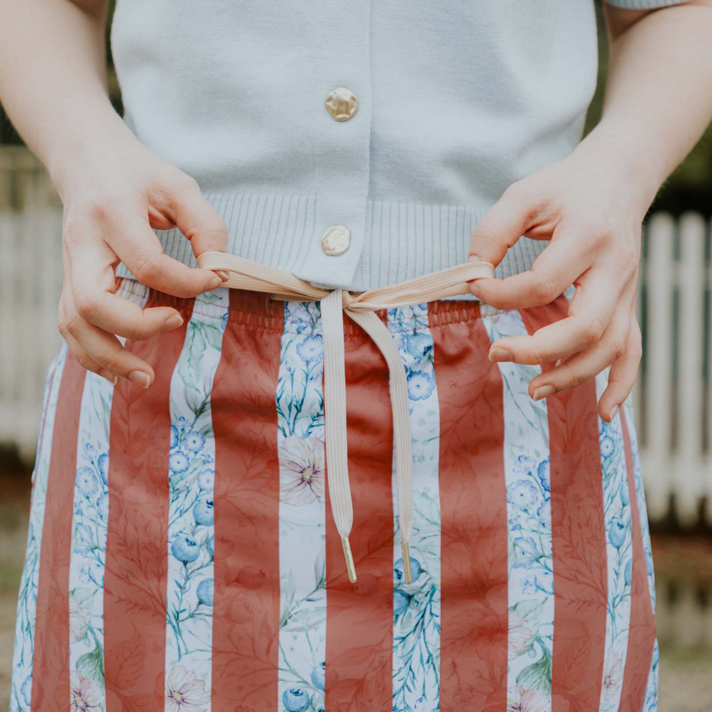 
                  
                    Person wearing a light blue shirt and striped skirt with floral patterns and drawstring
                  
                