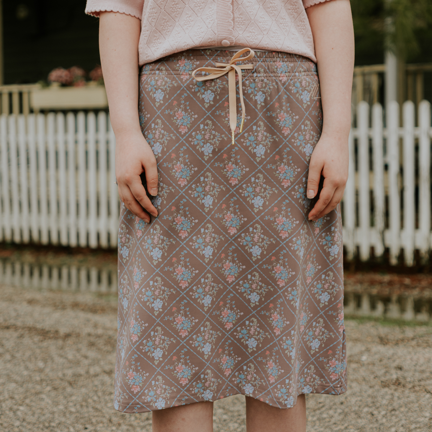 Person wearing a patterned skirt with a white picket fence in the background