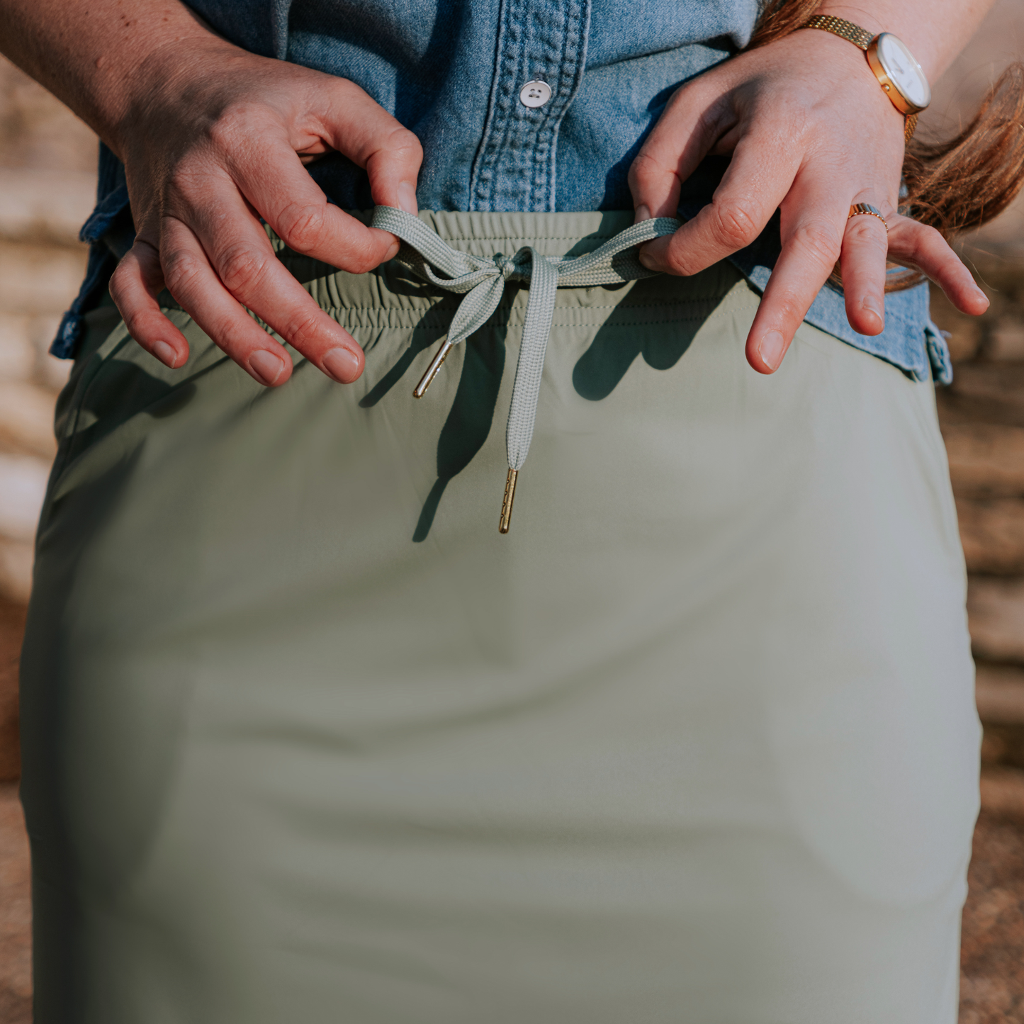 
                  
                    Person adjusting the drawstring of a green skirt with a blurred background
                  
                
