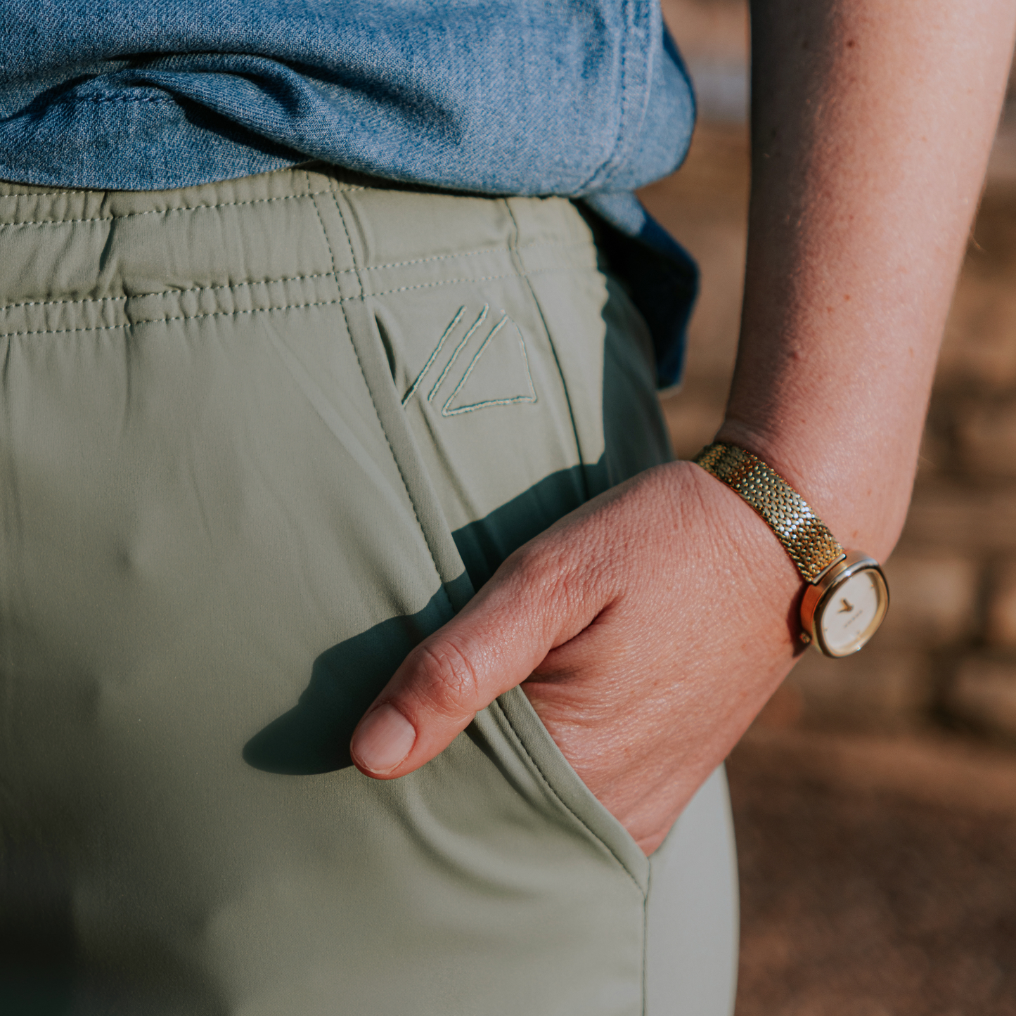 
                  
                    Person wearing green skirt with a brand logo and a gold watch, blurred background
                  
                