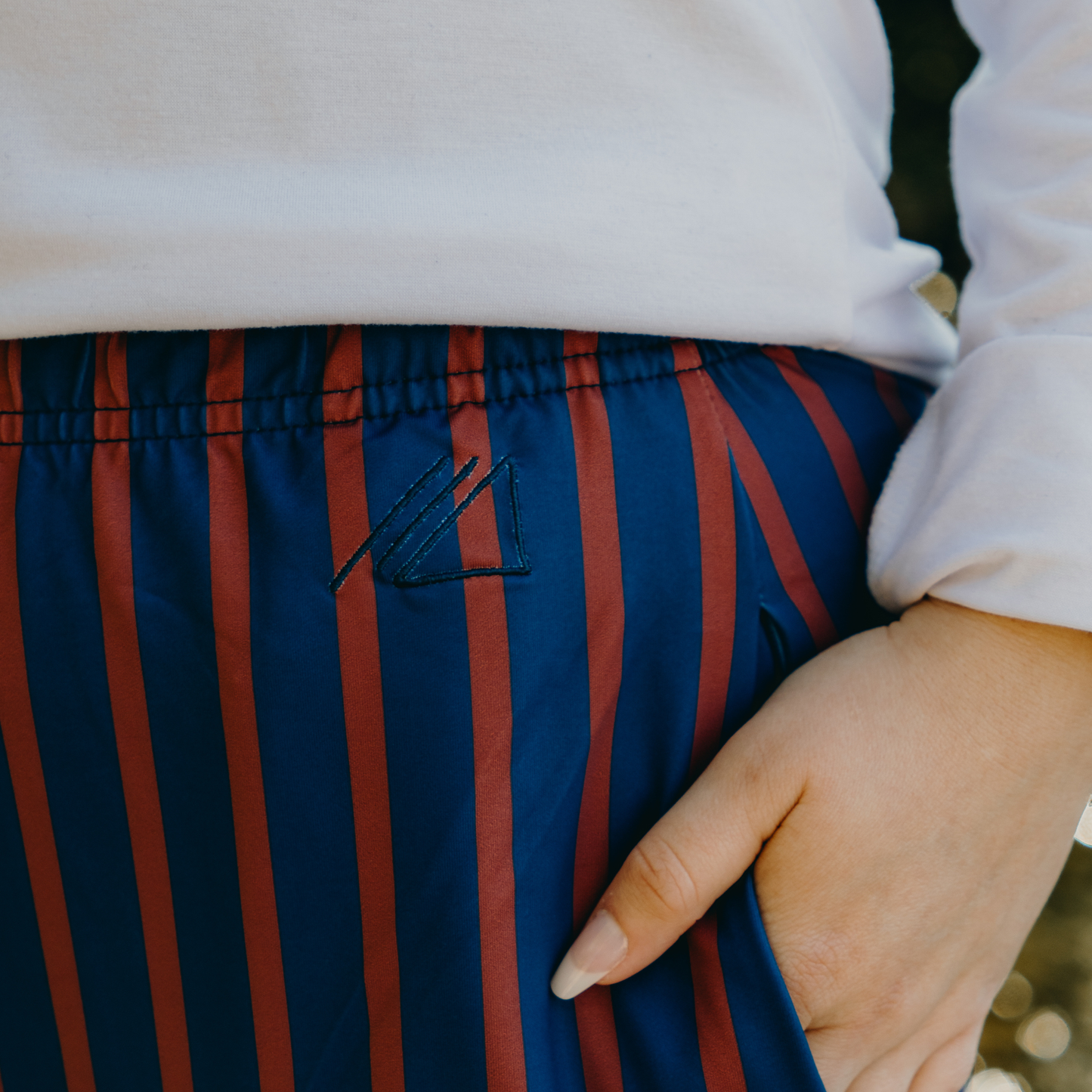 
                  
                    Close-up of blue and orange striped skirt with a brand logo, worn by a person.
                  
                