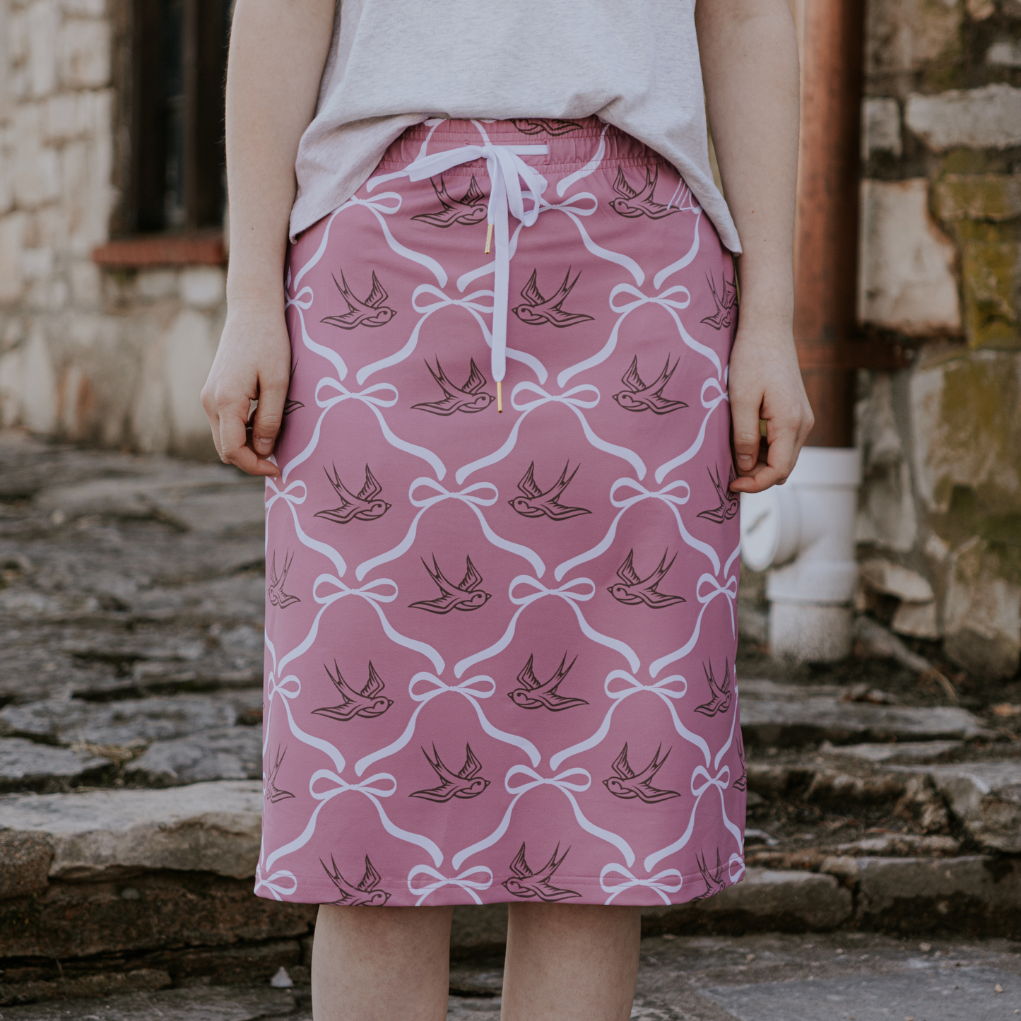 
                  
                    Person wearing a pink skirt with bird pattern in front of a stone wall.
                  
                