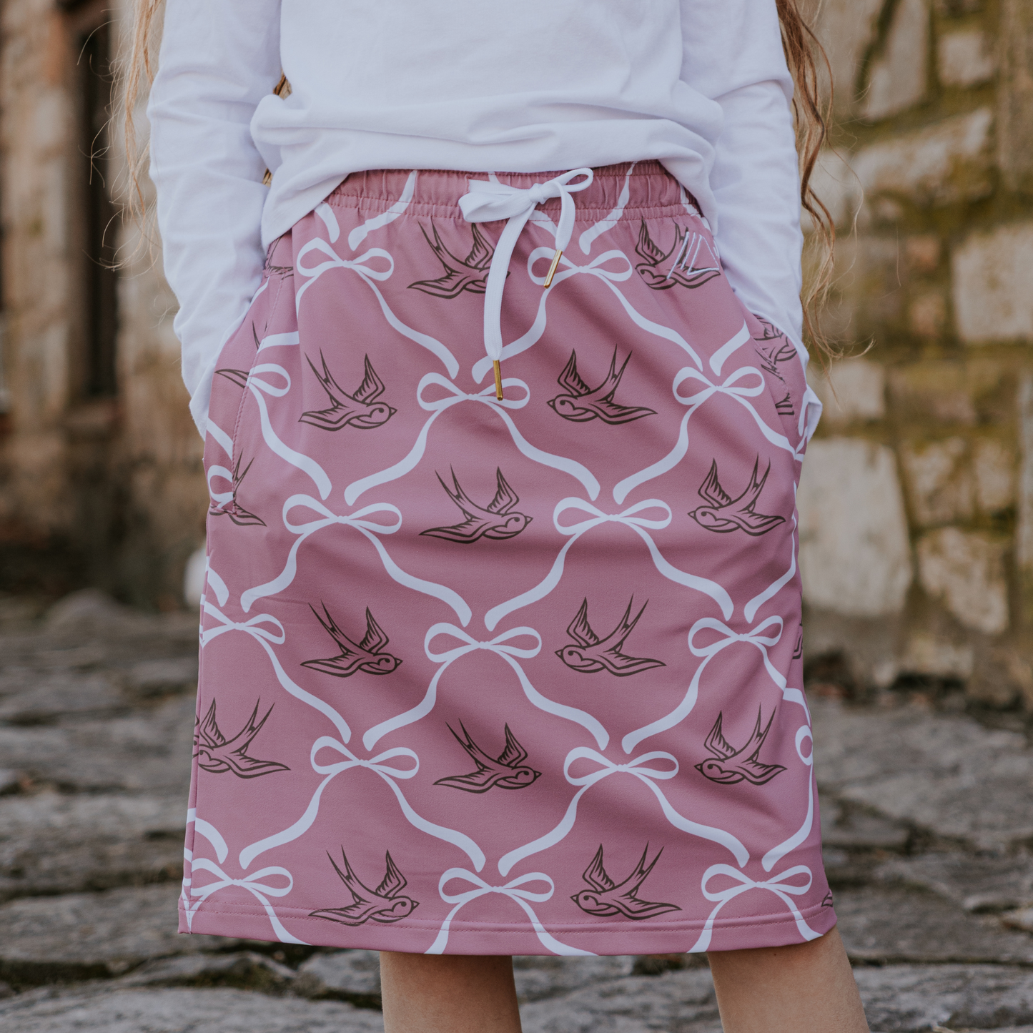 Pink skirt with bird and bow pattern worn by a person, blurred background