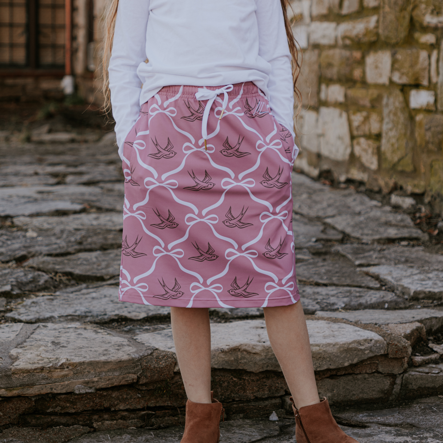 Person wearing a pink skirt with bird pattern standing on stone steps.