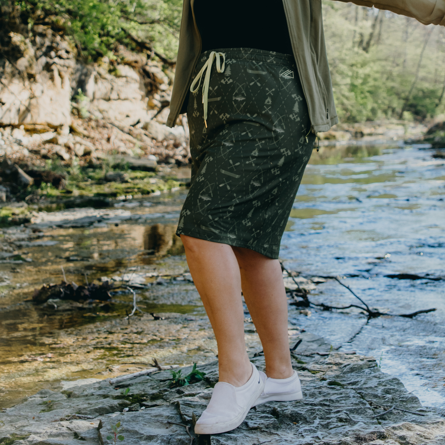 Person wearing a patterned skirt standing by a stream with a natural background