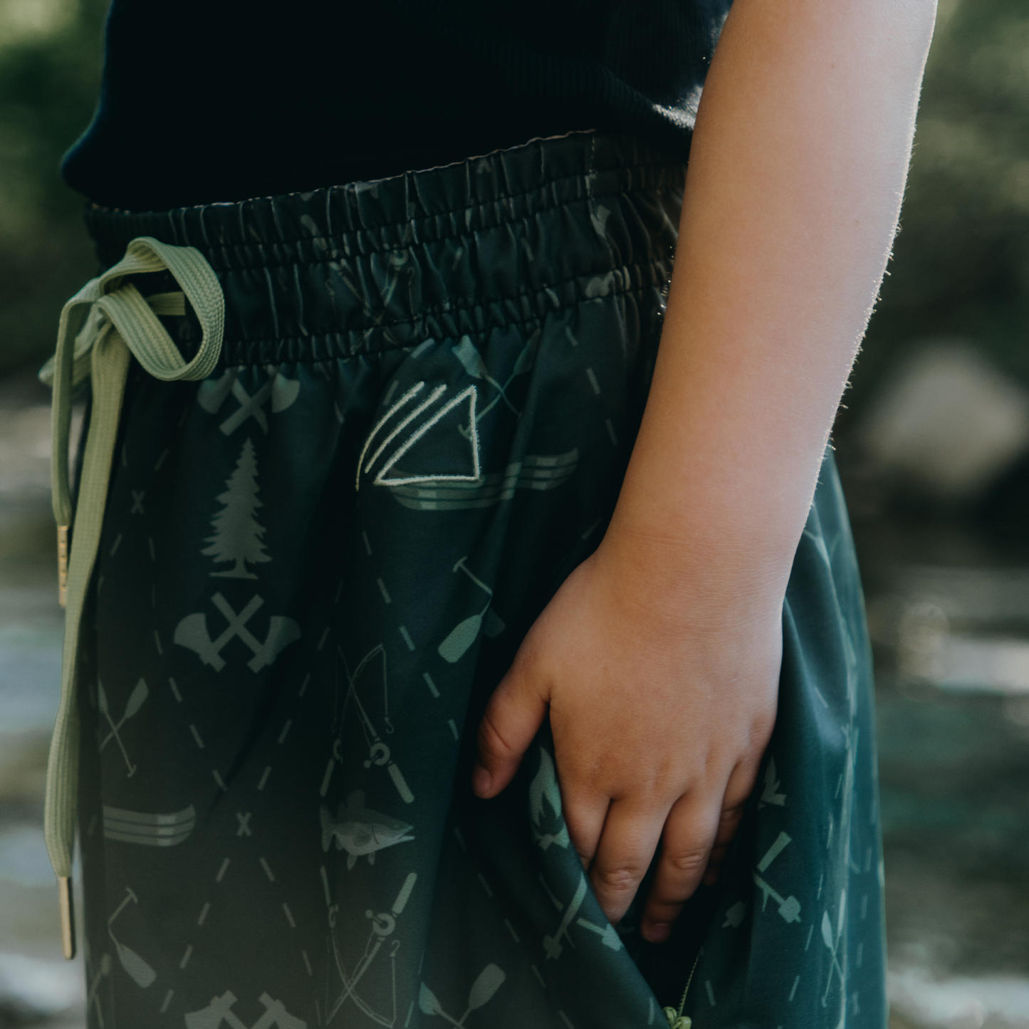 
                  
                    Kid wearing dark green skirt with nature-themed patterns, standing outdoors.
                  
                