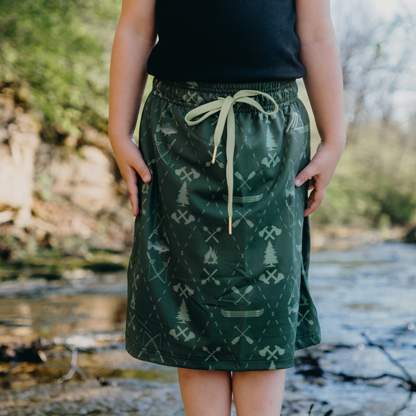 Kid wearing a green patterned skirt with a natural background